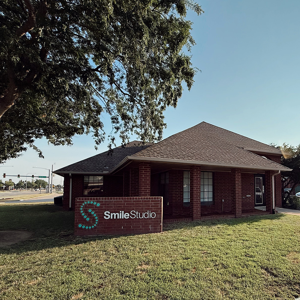 The image shows a building with a sign that reads Smile Studio, indicating it s a dental practice, set against a clear sky with some clouds and trees in the background.